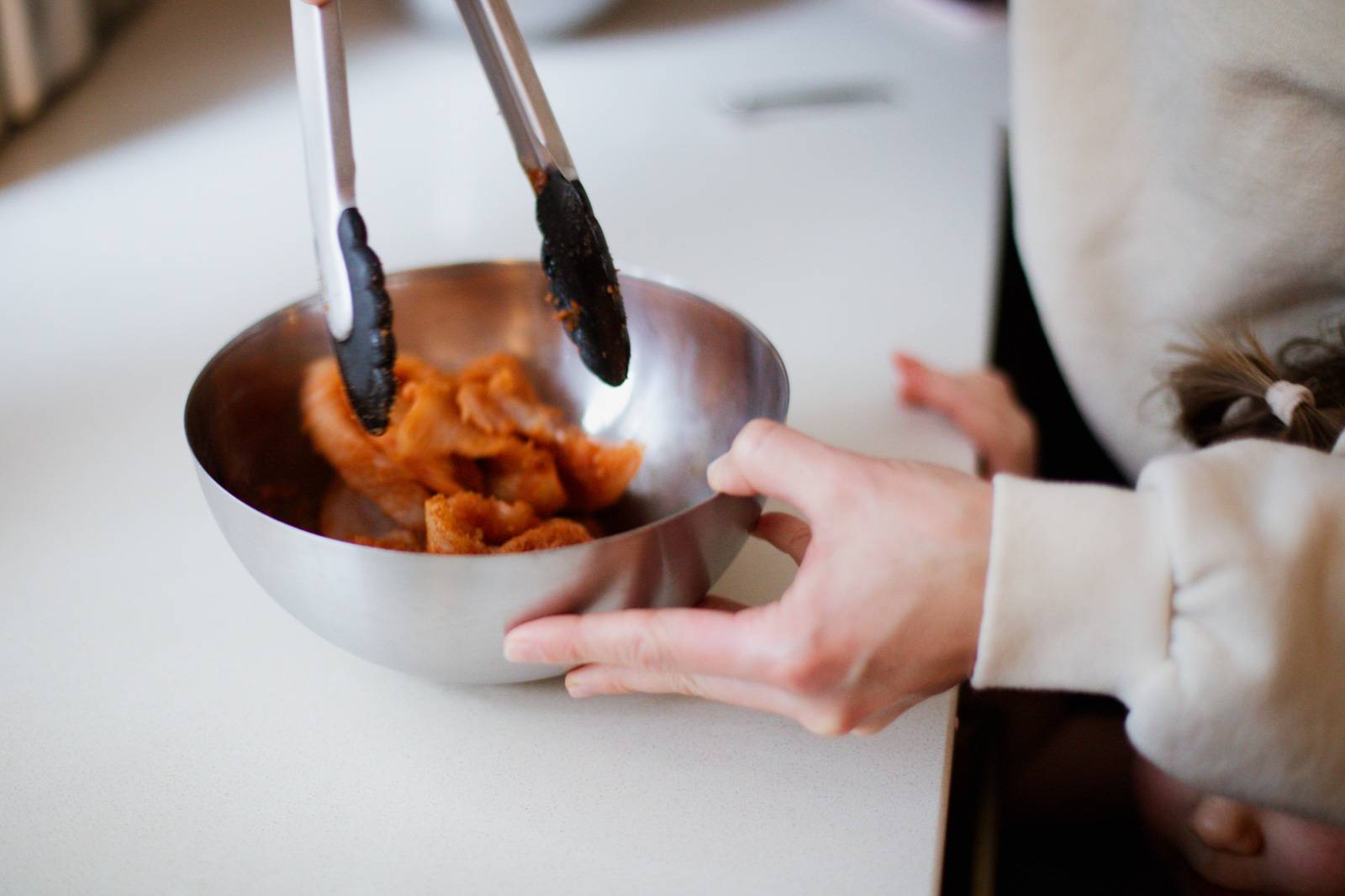 Tossing chicken with spices in a bowl.