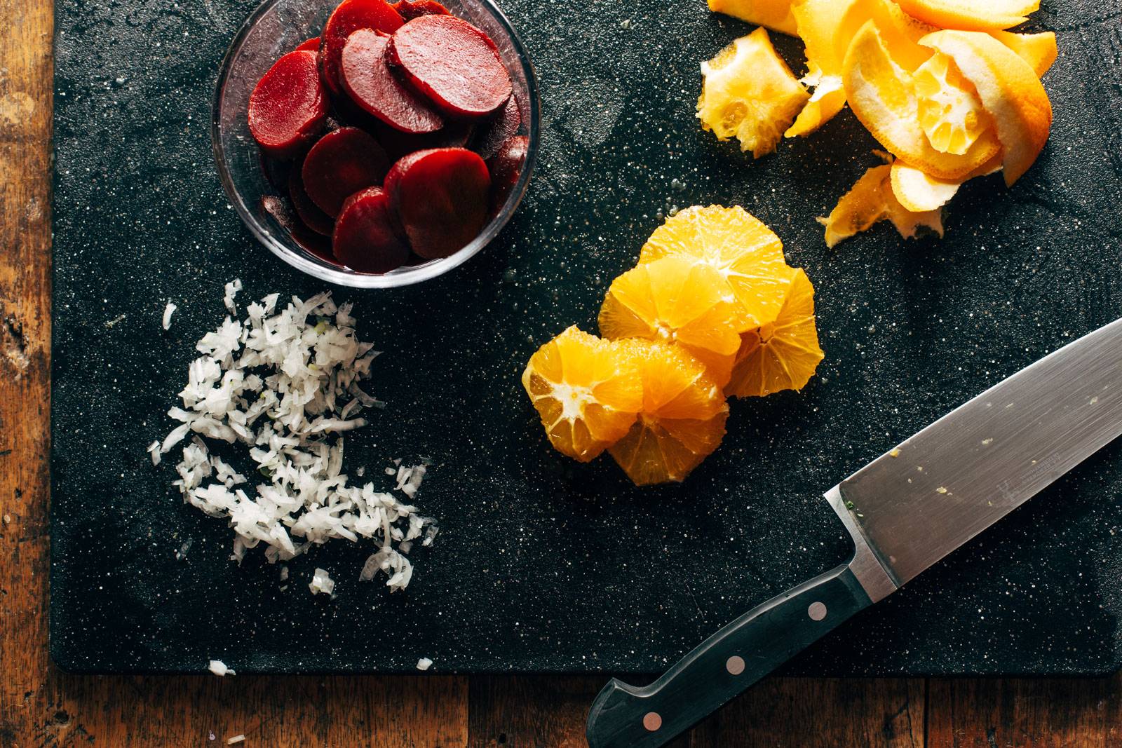 Cutting oranges, beets, and shallots on a cutting board.