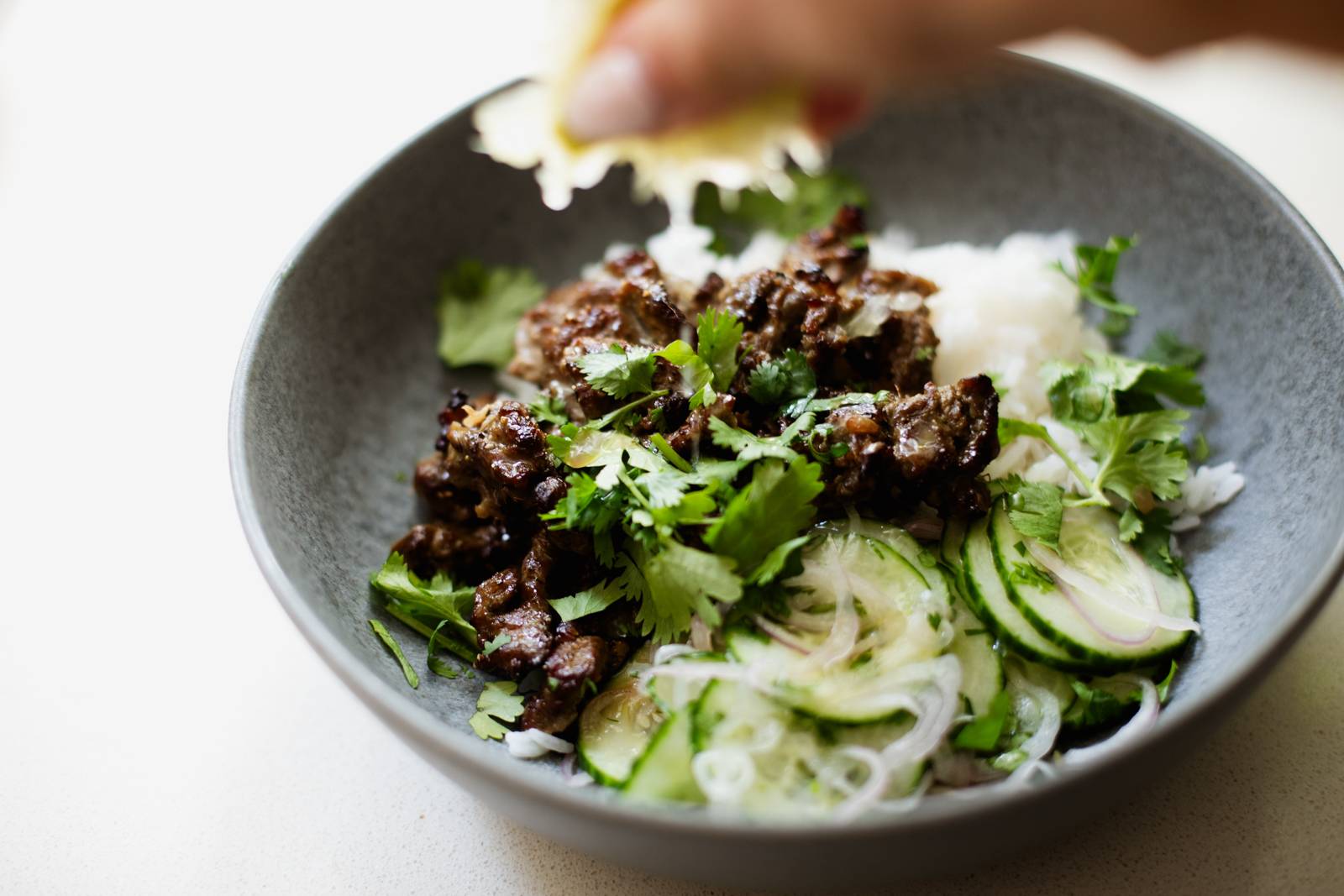 Squeezing lime on a bowl of steak, rice, and cucumber salad.