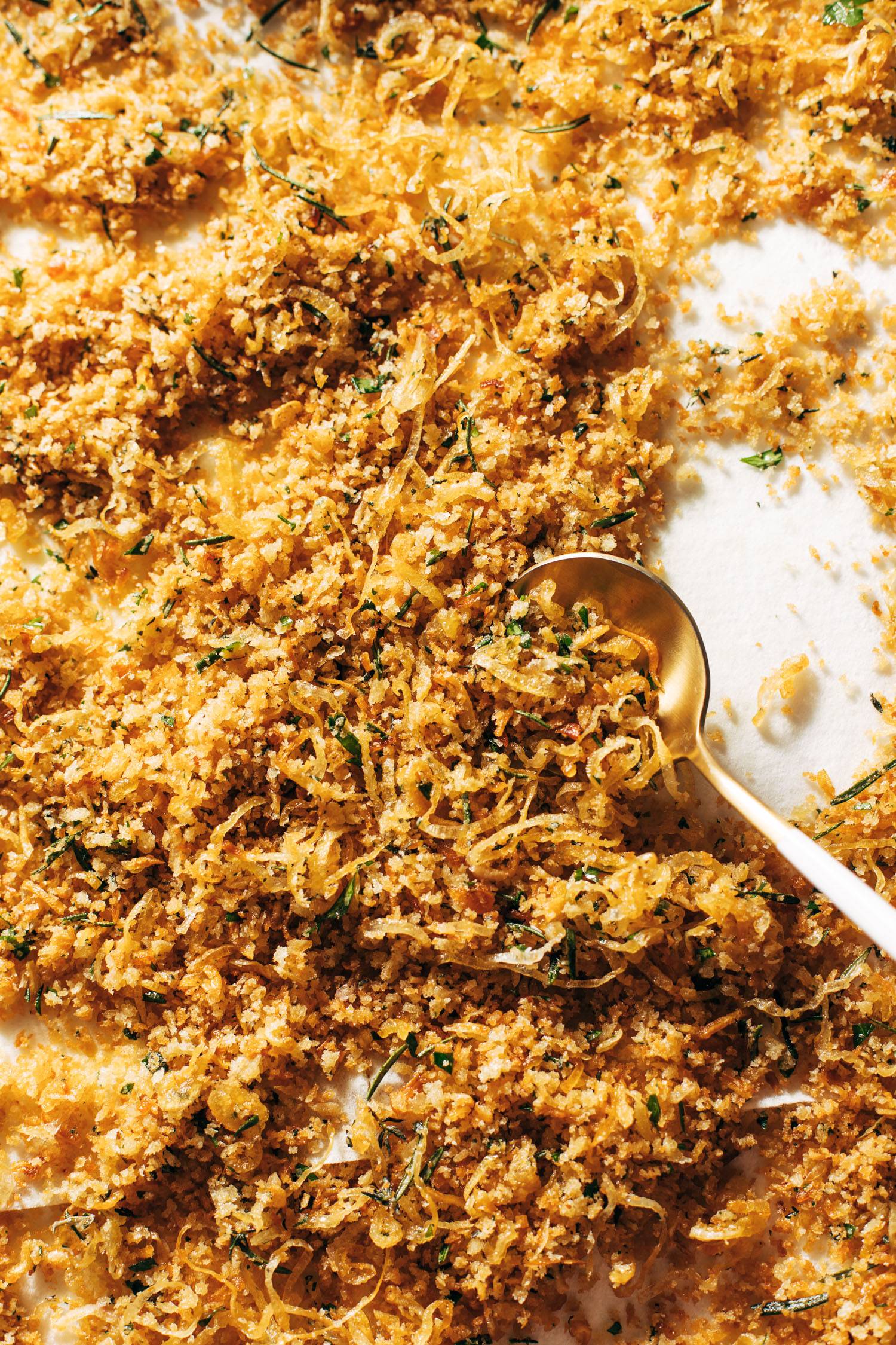 Golden breadcrumbs on a sheet pan with a spoon.