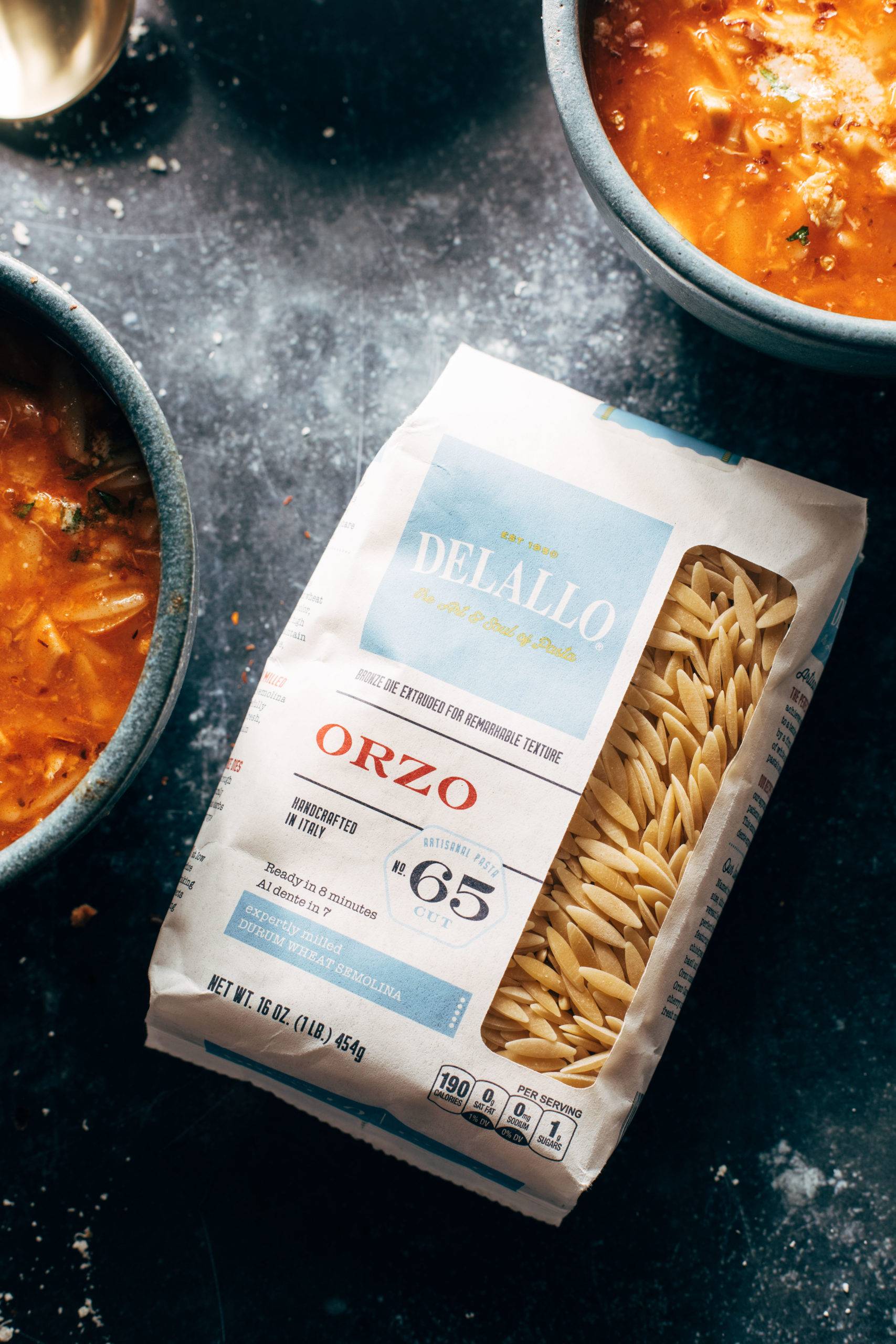 Package of orzo pasta next to a bowl of soup