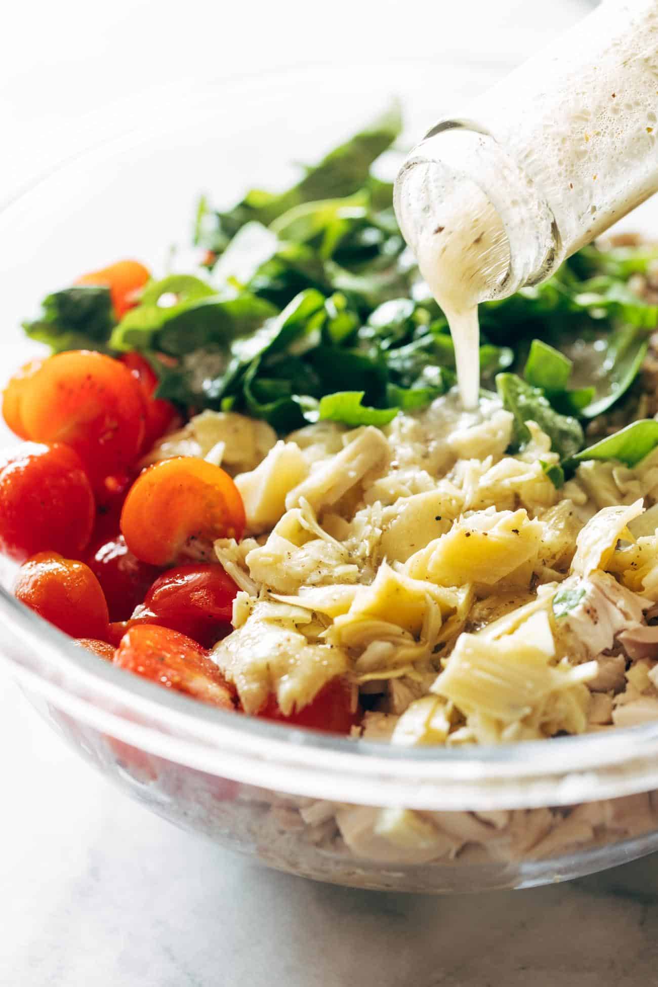 Dressing being poured on chicken quinoa salad