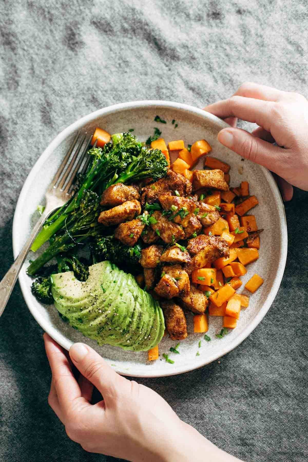 Chicken and sweet potato in a bowl with a fork. A white hand is holding the bowl. 