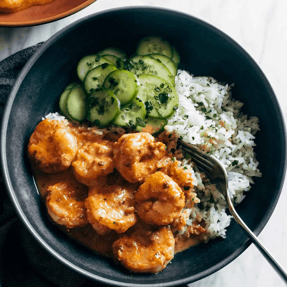 Chipotle orange shrimp in a bowl with rice and cucumbers.