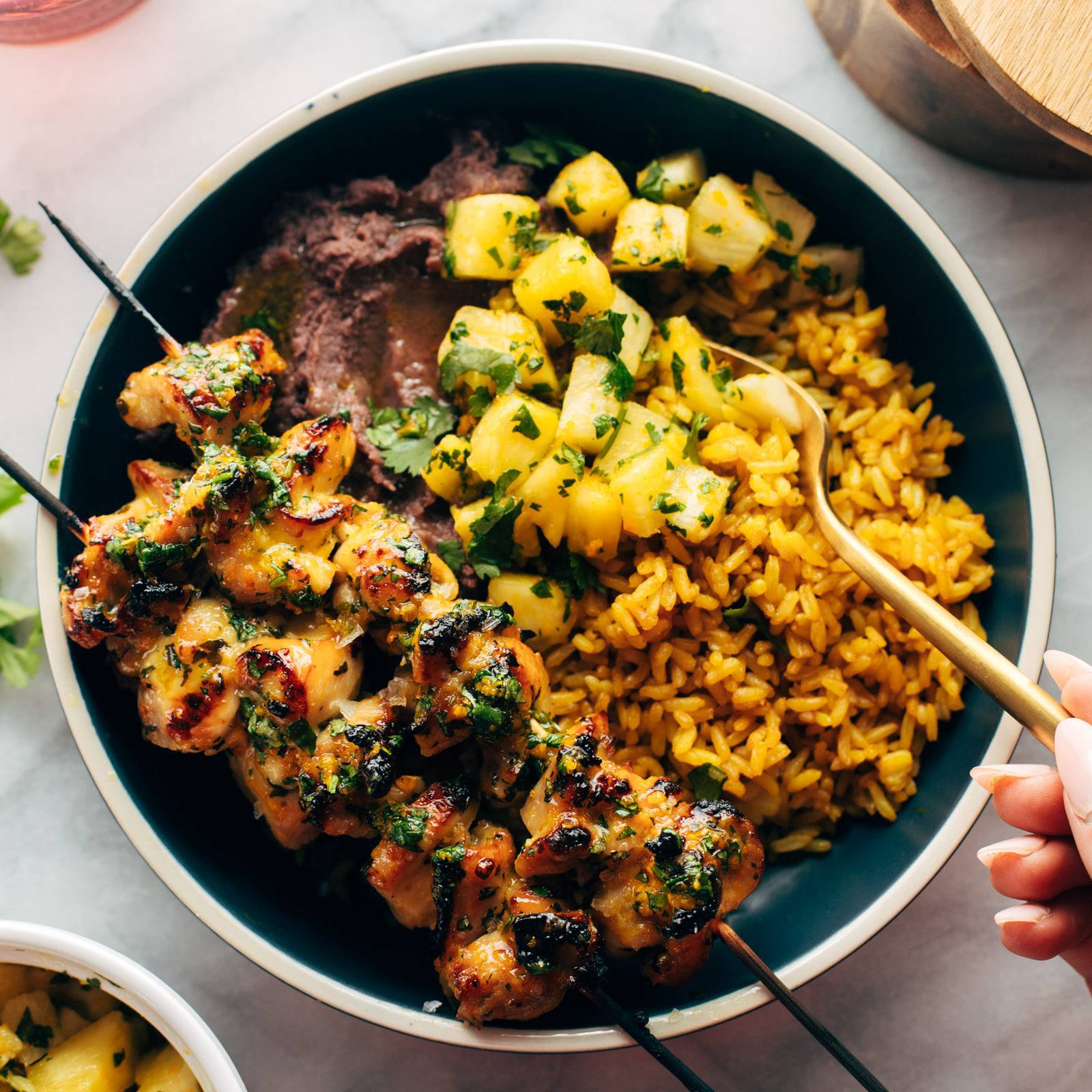 Cilantro Orange Chicken in a bowl with rice, beans, and pineapple.