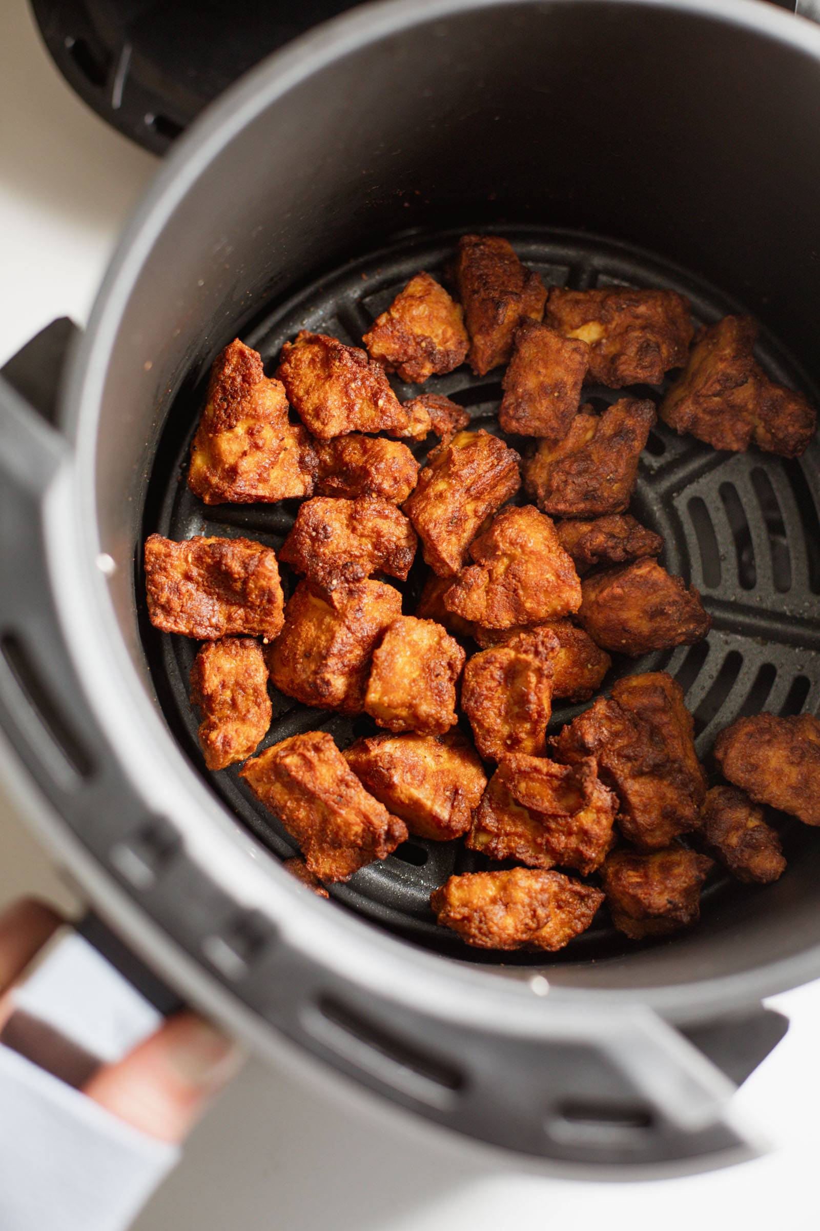 Seasoned tofu in the basket of an air fryer.