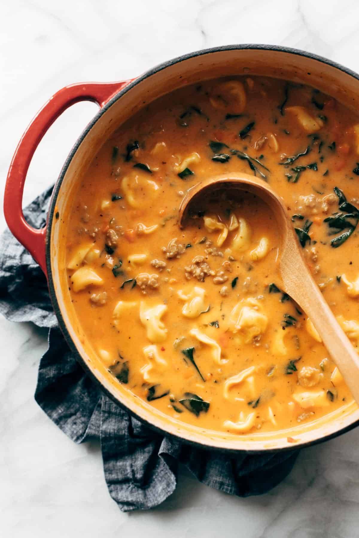 Tortellini soup in a pot with a ladle.