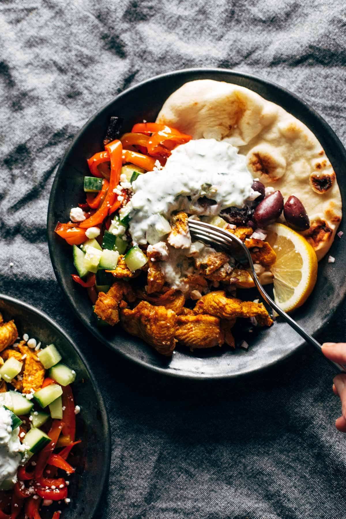 A plate of chicken, red bell peppers, cucumber, and tzatziki sauce with a lemon wedge.