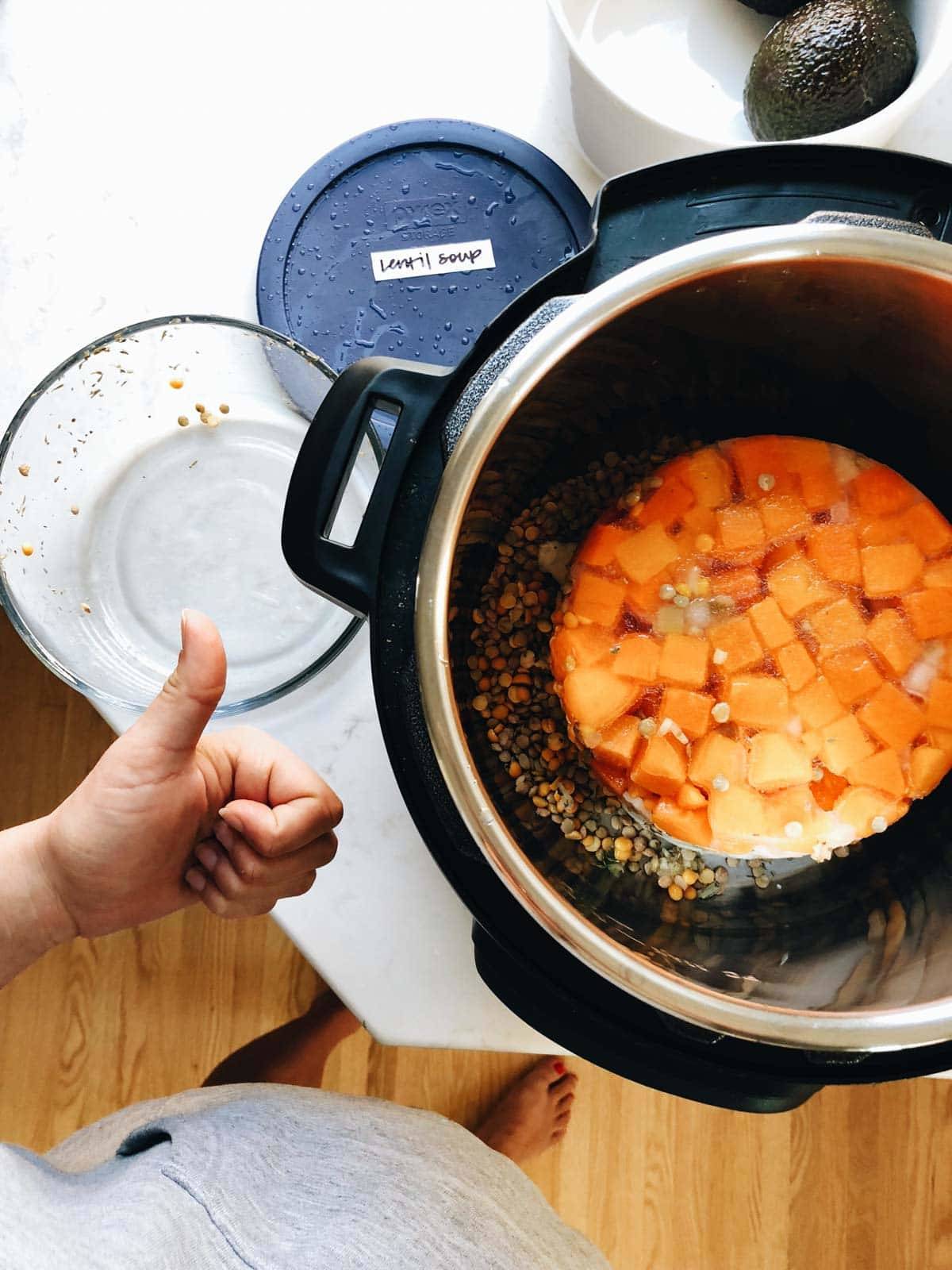 White hand giving a thumbs up next to an Instant Pot cooking a freezer meal from frozen. 