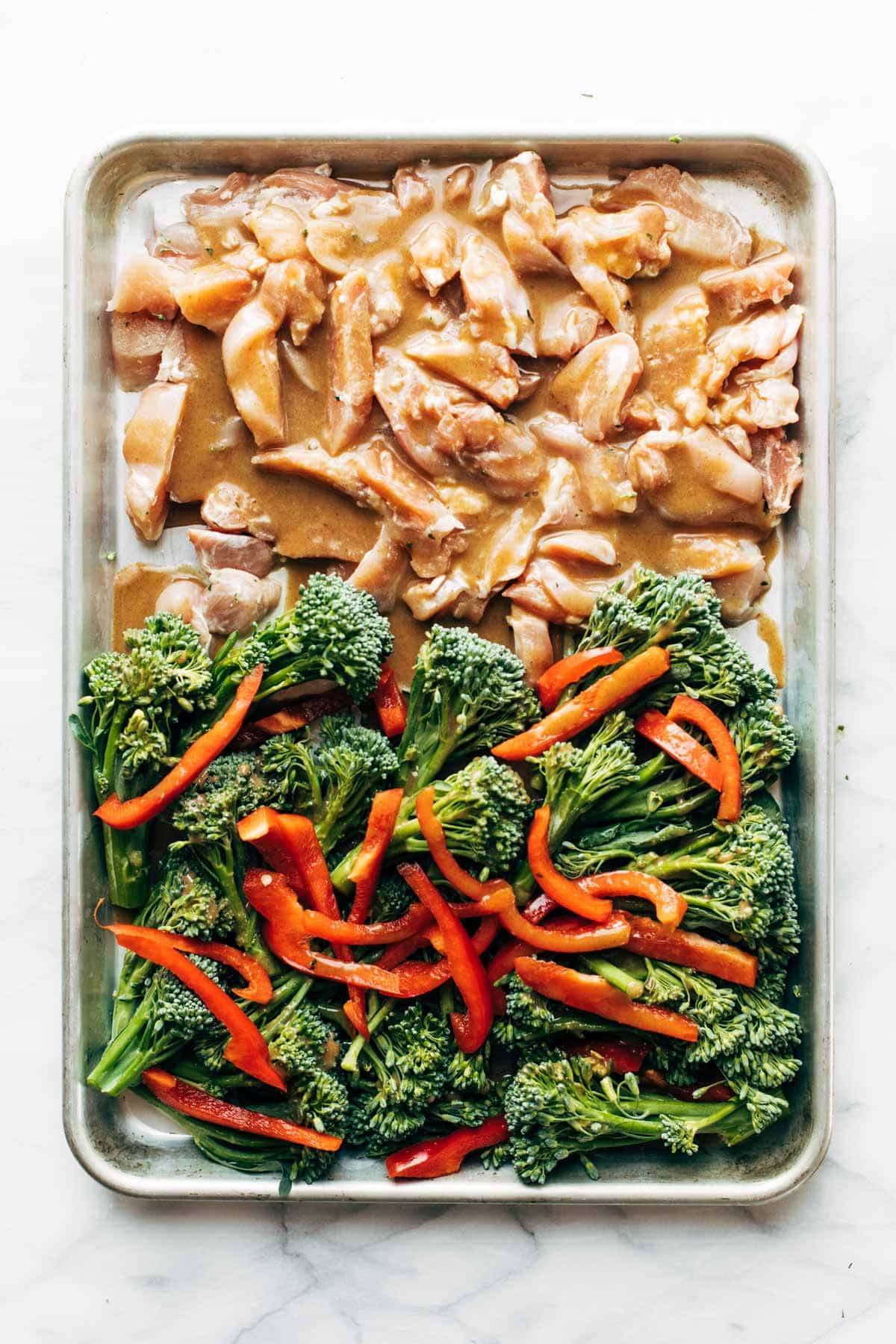 Raw chicken and veggies on a sheet pan.