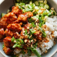 Gochujang tofu in a bowl with rice, peanuts, and herbs.