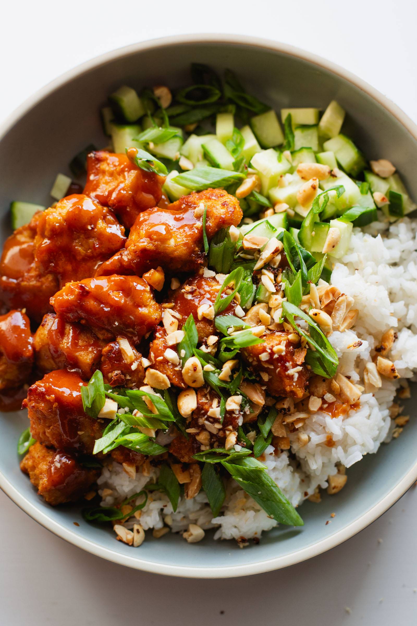 Gochujang tofu in a bowl with rice, peanuts, herbs, and cucumbers.