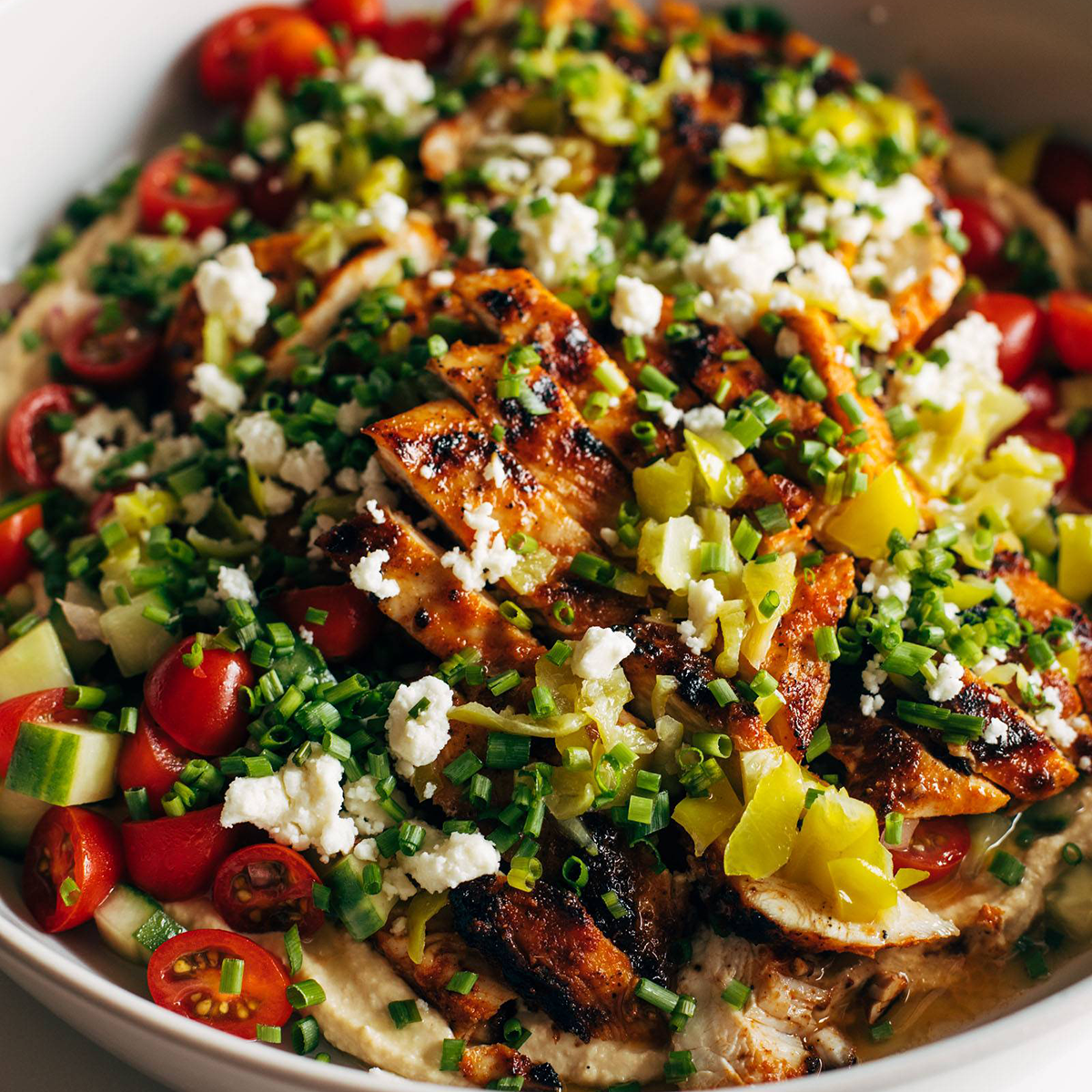 Grilled chicken on top of hummus and tomato salad.