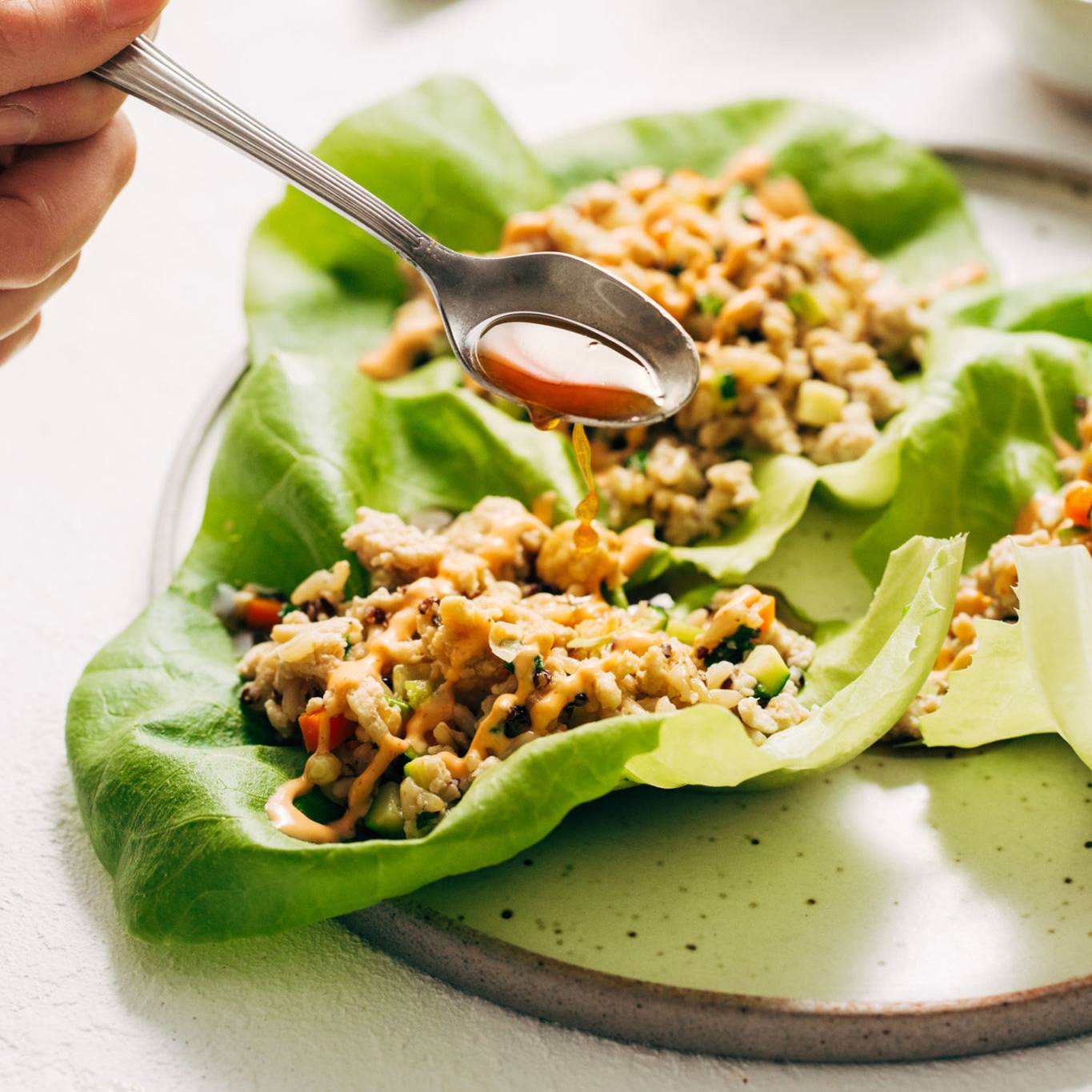 Spoon ladeling lime sauce on the chicken lettuce cups on a plate.