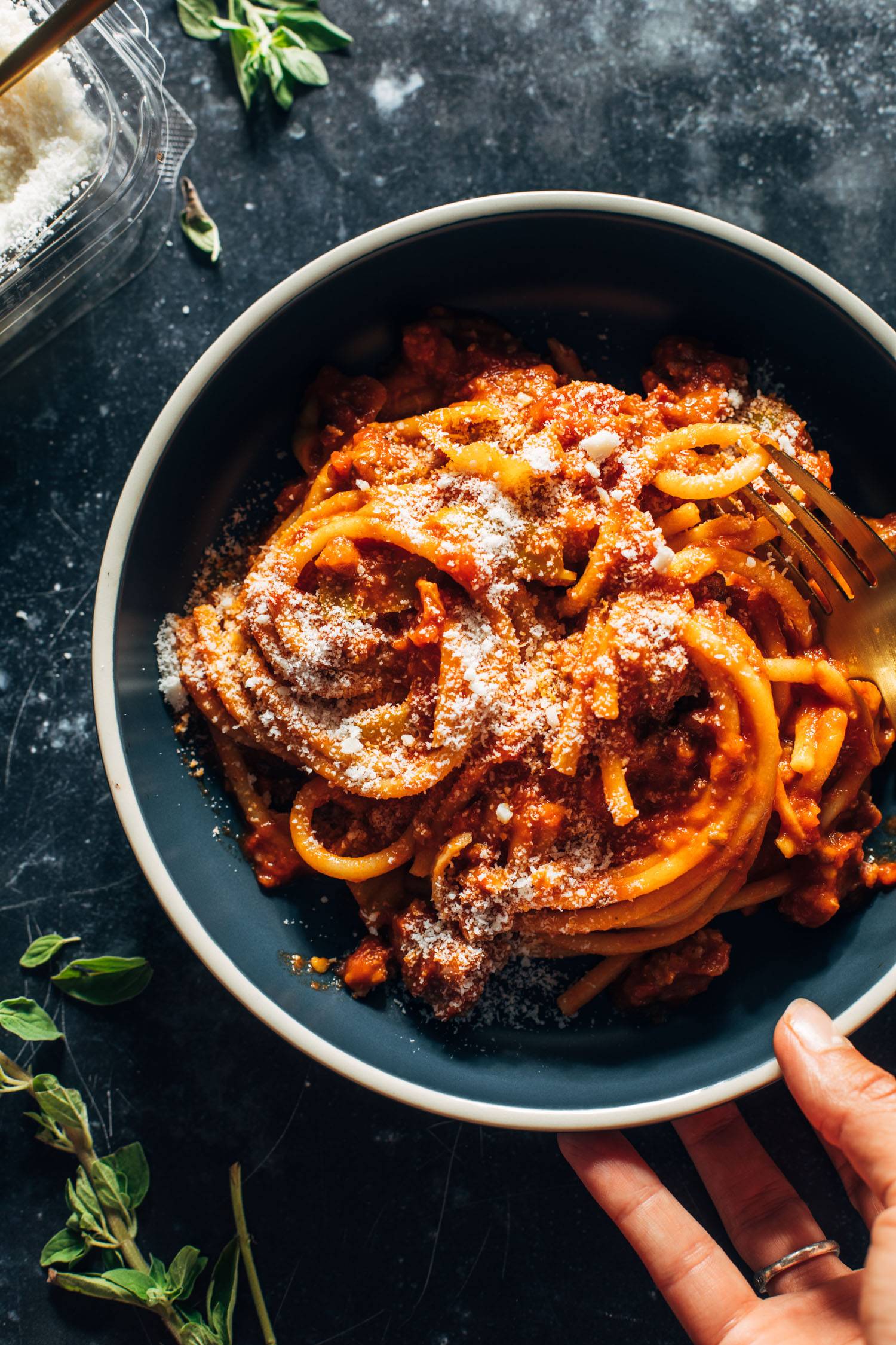 Bucatini in a bowl with red sauce and pecorino on top.