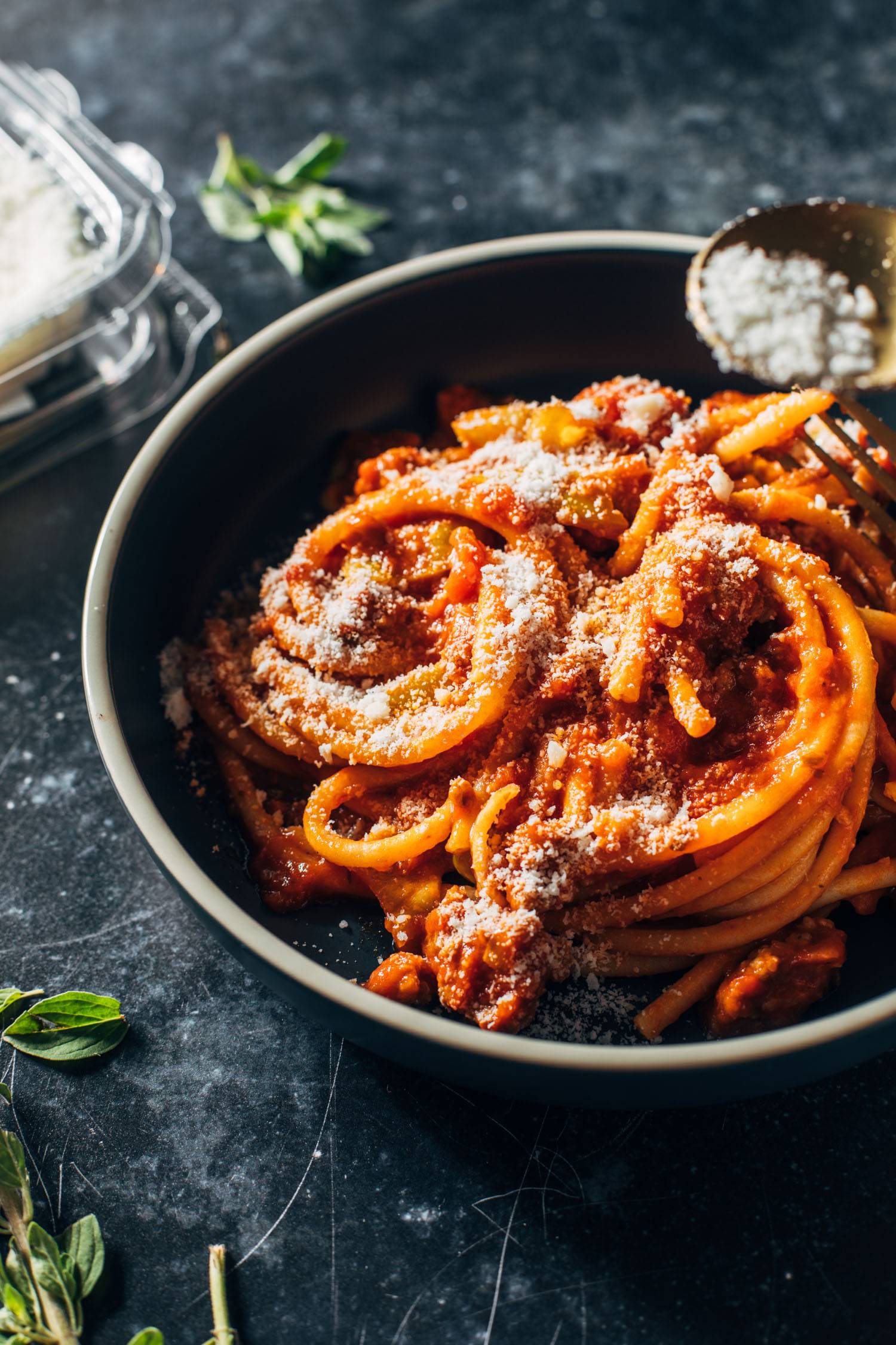 Sprinkling pecorino on top of bucatini with red sauce.