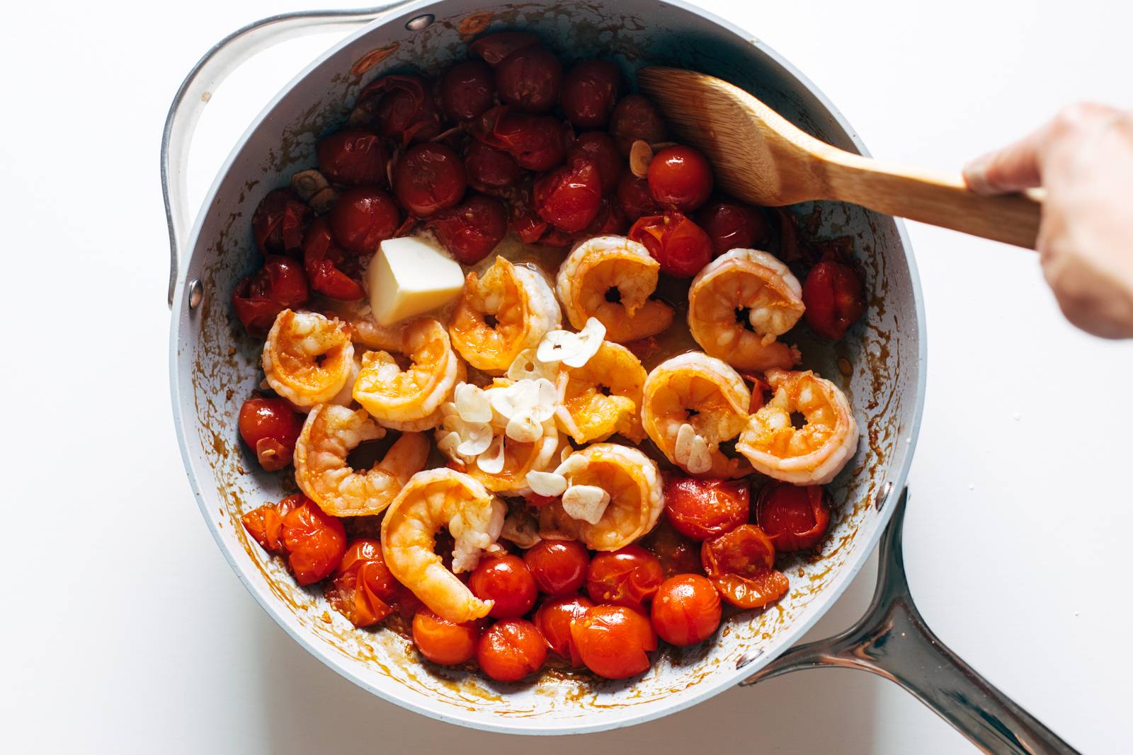 Butter and garlic being added to a pan with shrimp and tomatoes