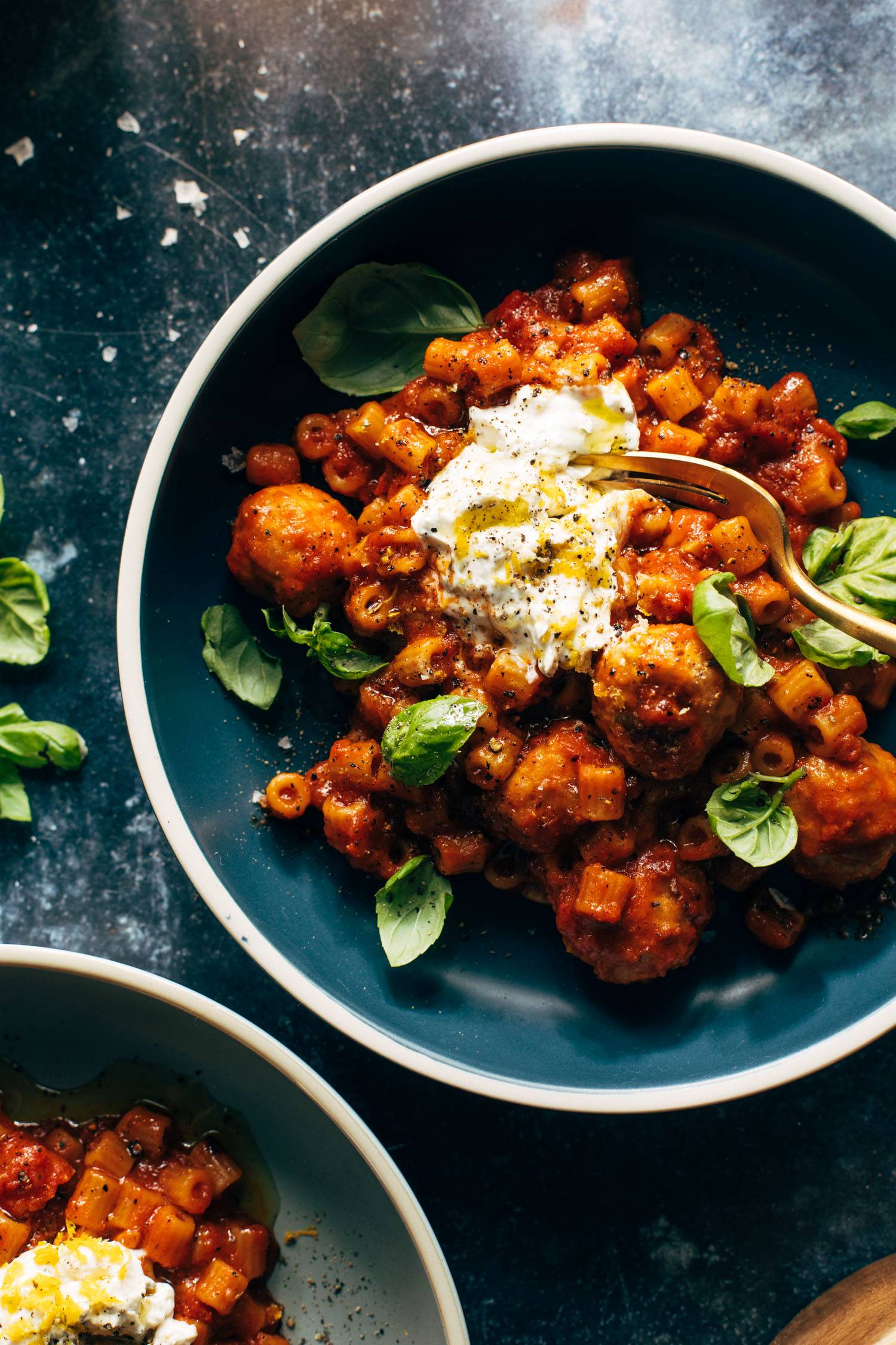 Ditalini pasta and meatballs in red sauce on a plate, topped with creamy ricotta.