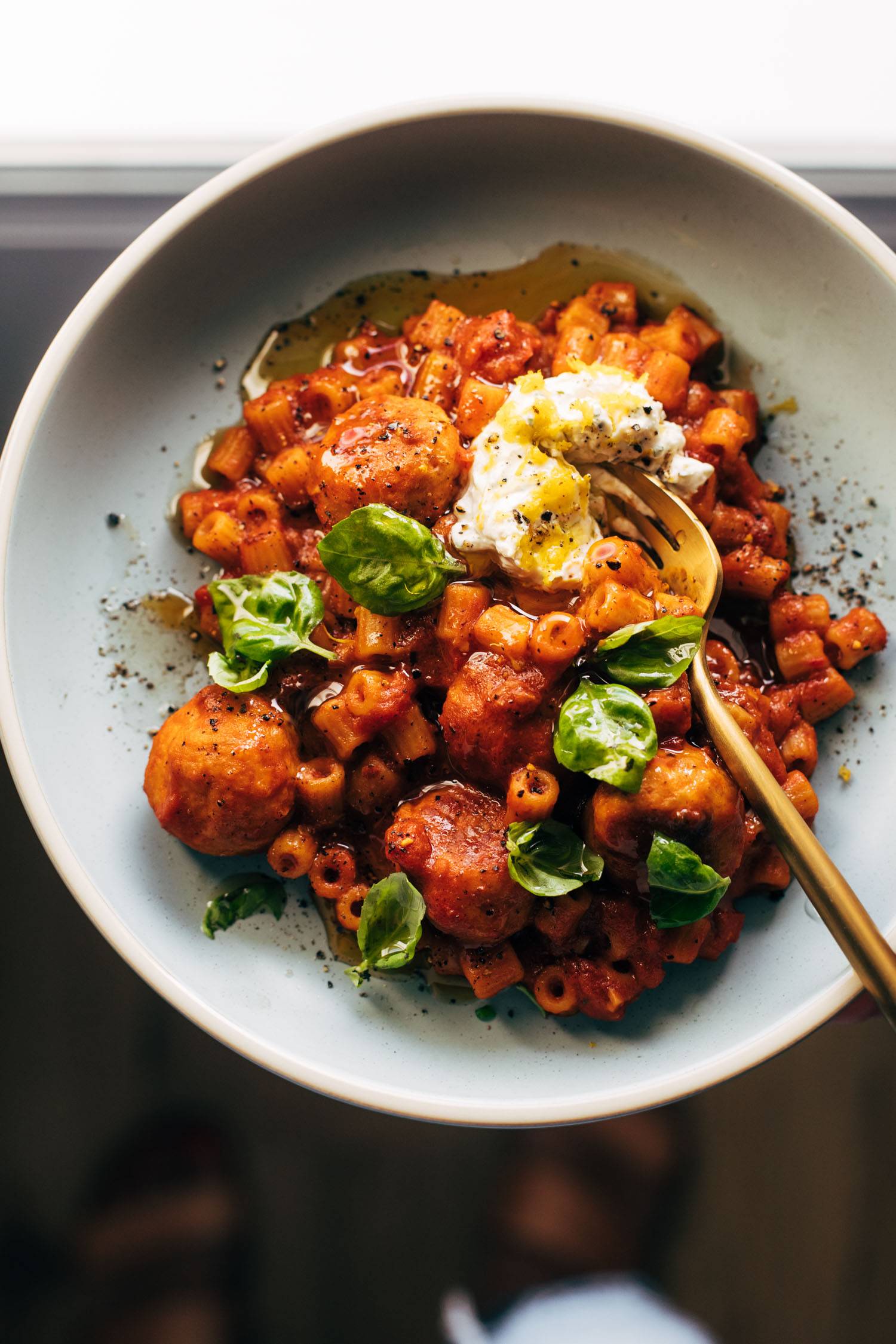 Pasta and meatballs on a plate with ricotta and a fork.