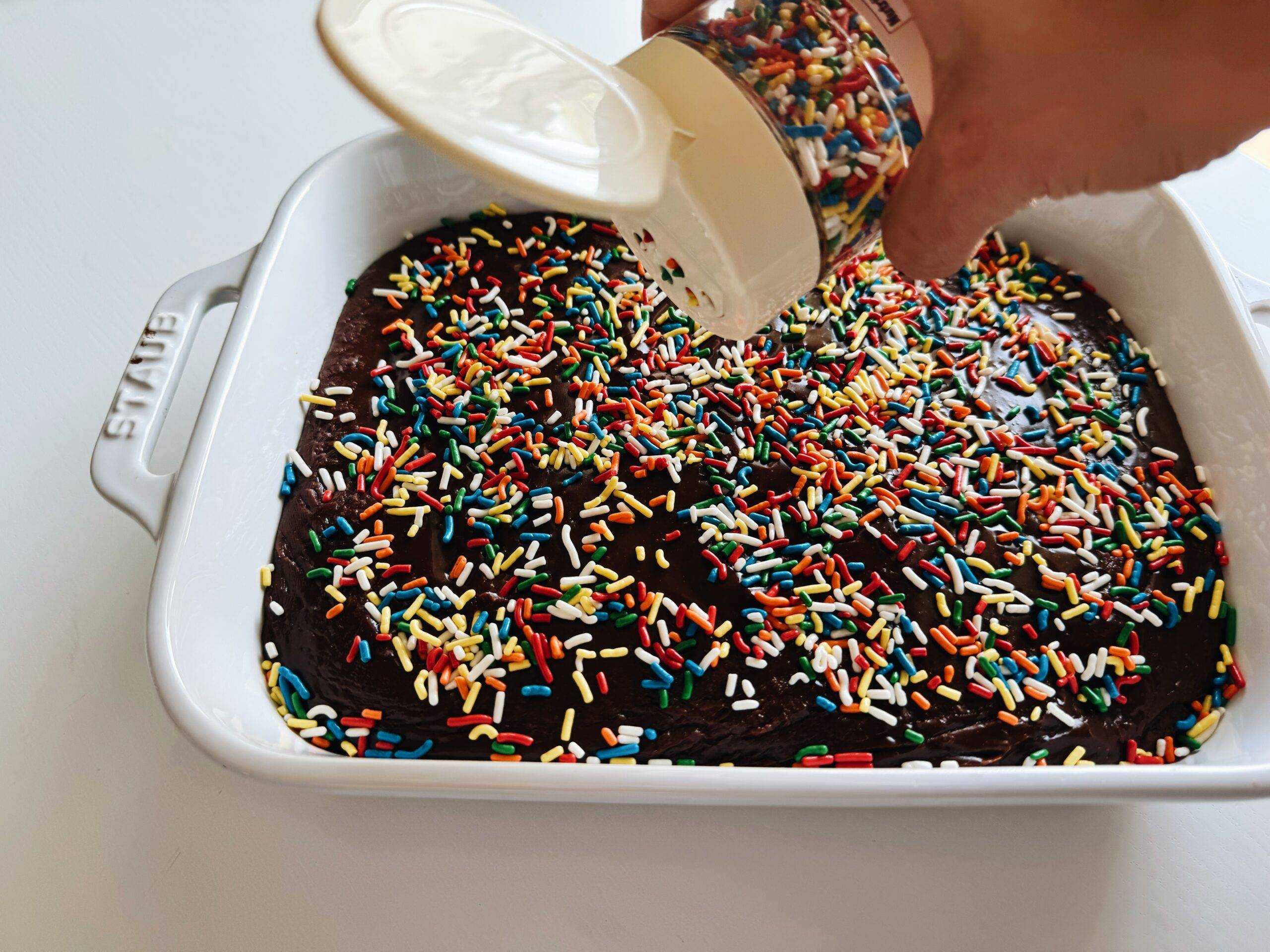 Sprinkling sprinkles on top of a pan of brownies.