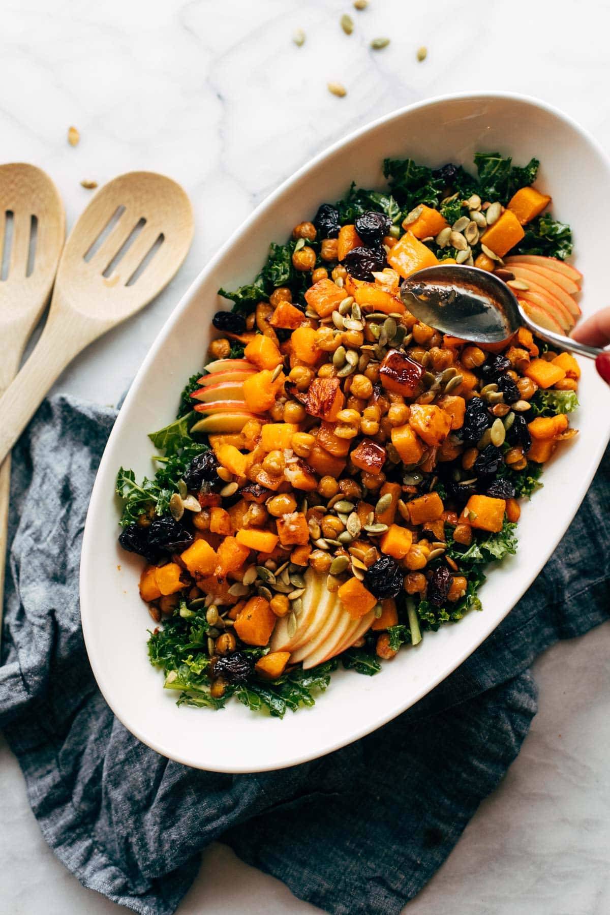 Drizzling dressing over squash salad in a serving dish.