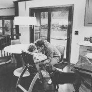 A man sitting on a chair facing a baby who is having food.