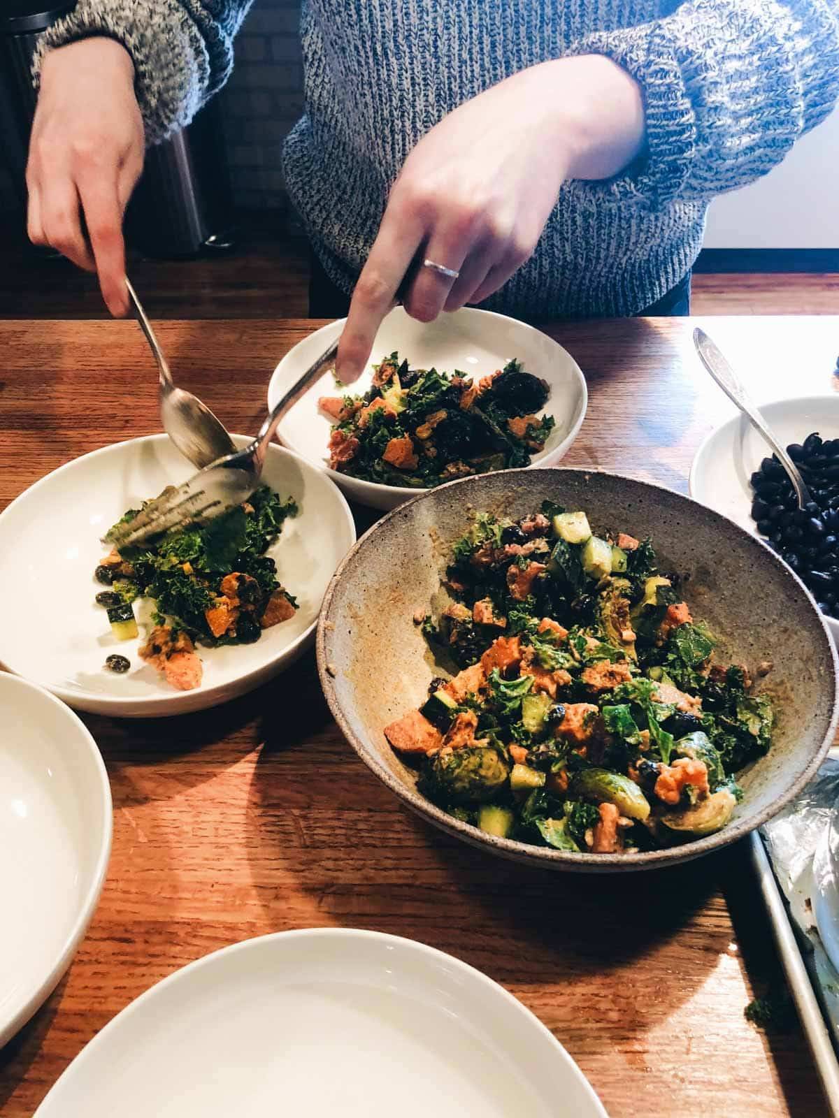 Hands serving Sunflower Salad into individual bowls.