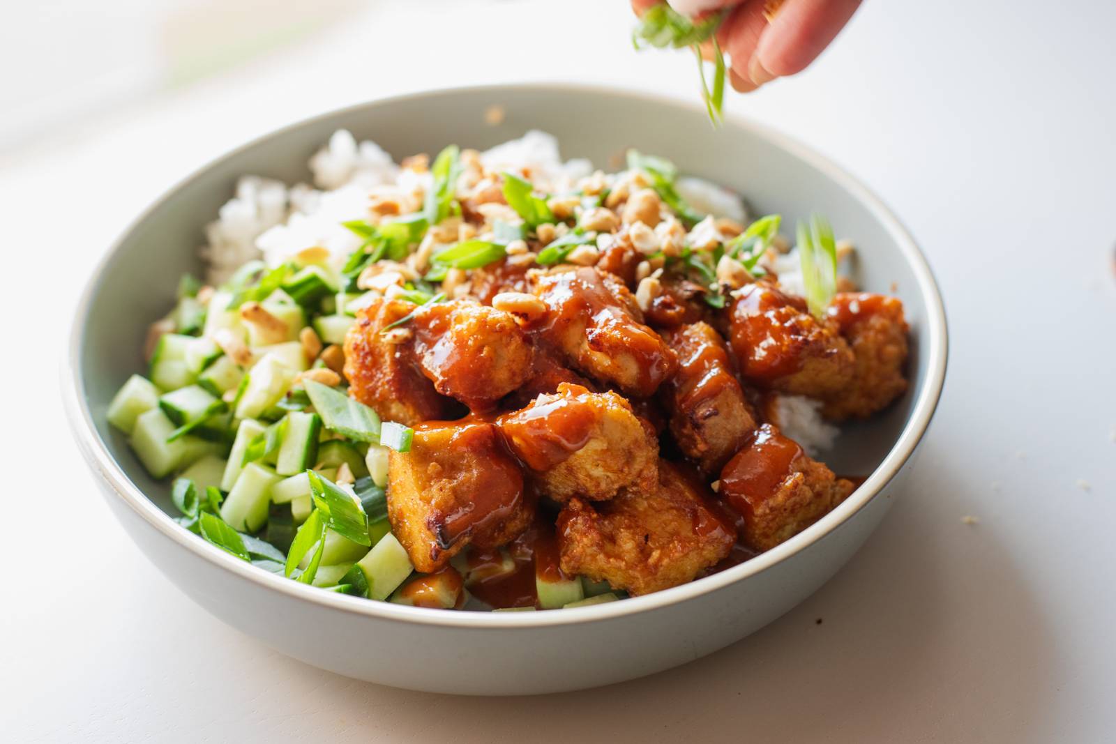 Sprinkling herbs on a bowl of tofu and rice.