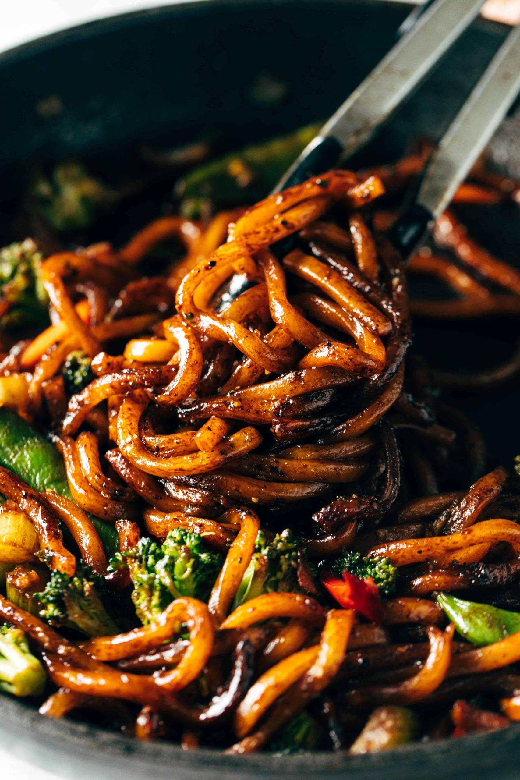 Tongs grabbing black pepper stir fried udon