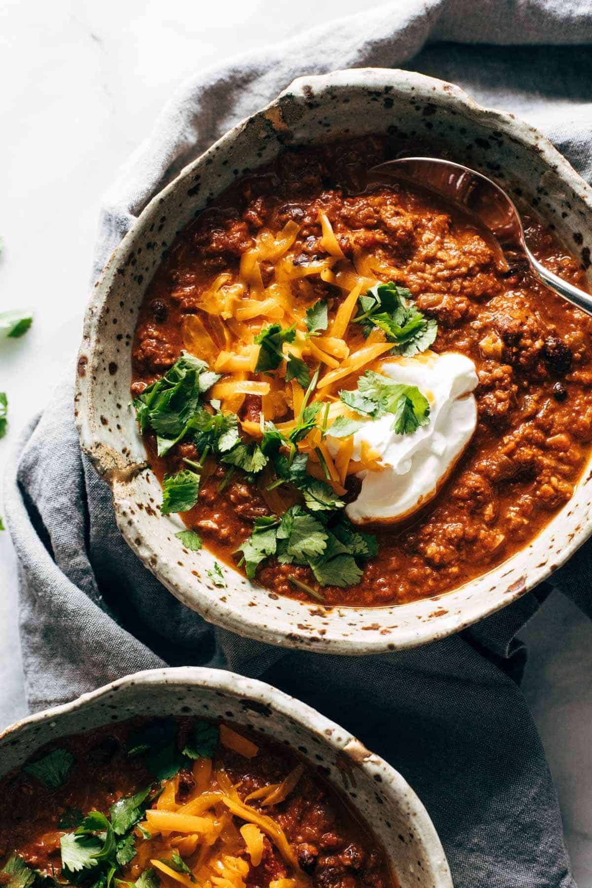 Bowls of chili with shredded cheddar, cilantro, and sour cream.