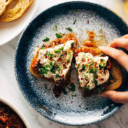 White hand grabbing zaalouk toast on a plate