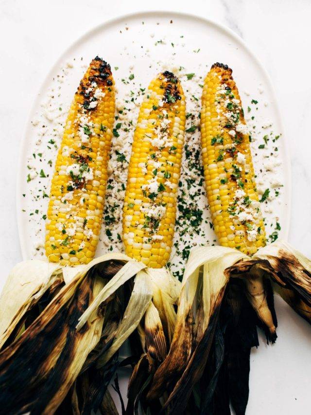 Grilled corn on a plate with cotija cheese.